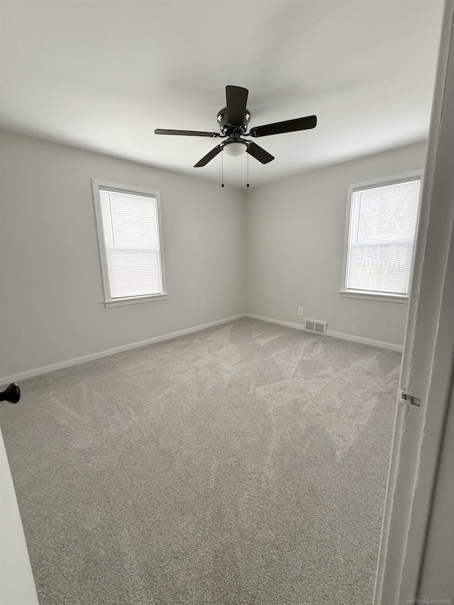 carpeted spare room featuring baseboards, plenty of natural light, a ceiling fan, and visible vents