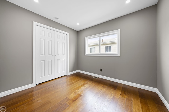 unfurnished bedroom with recessed lighting, baseboards, wood finished floors, visible vents, and a closet