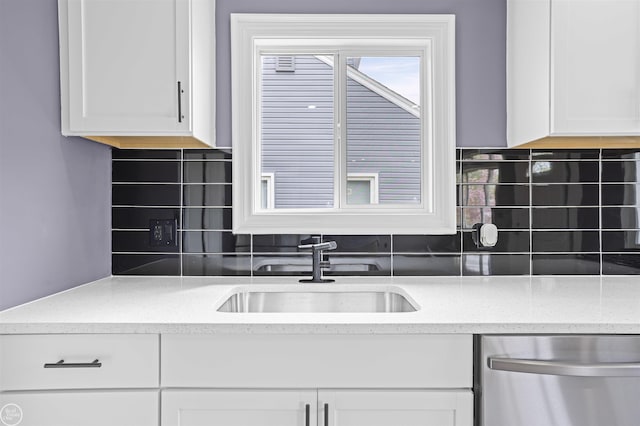 kitchen with backsplash, stainless steel dishwasher, a sink, light stone counters, and white cabinetry