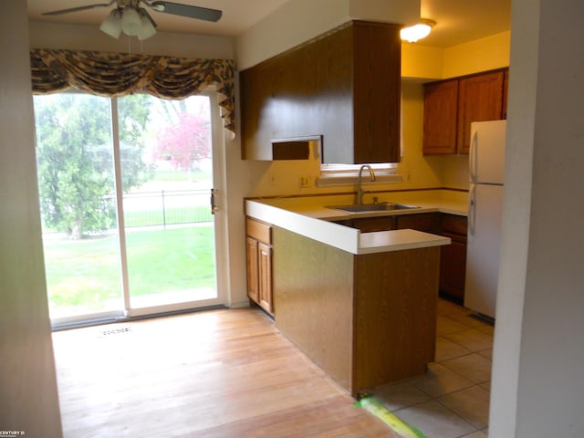 kitchen featuring freestanding refrigerator, a ceiling fan, a peninsula, brown cabinets, and a sink