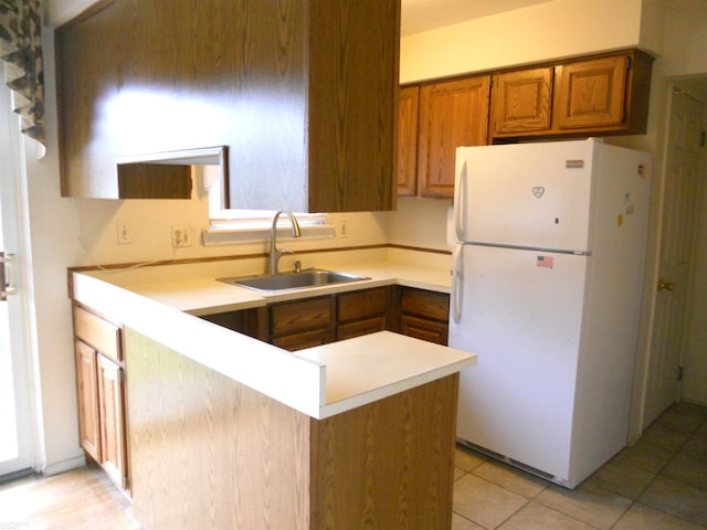 kitchen featuring brown cabinetry, a sink, light countertops, freestanding refrigerator, and a peninsula