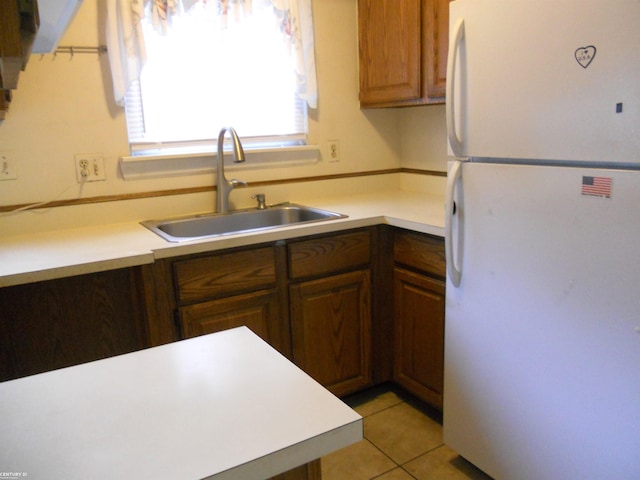 kitchen featuring freestanding refrigerator, light tile patterned floors, a sink, and light countertops