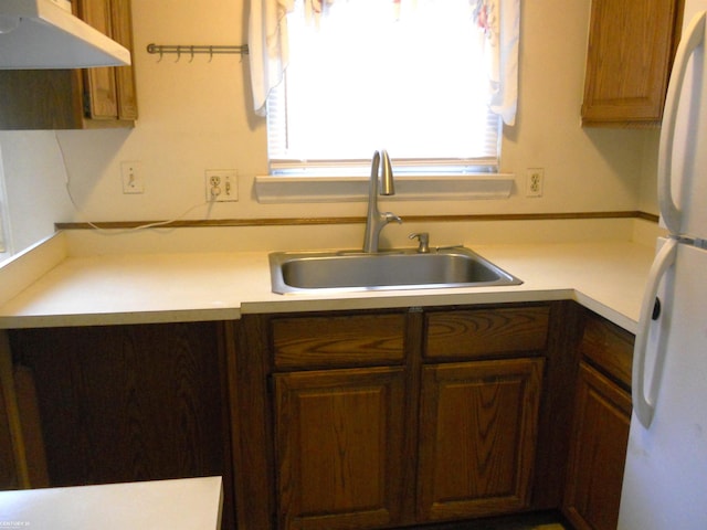 kitchen featuring a sink, light countertops, freestanding refrigerator, and under cabinet range hood