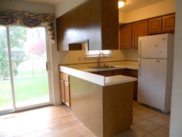 kitchen featuring a sink, light countertops, brown cabinetry, freestanding refrigerator, and a peninsula
