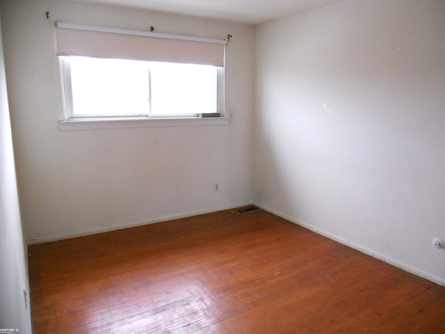 empty room with visible vents, a wealth of natural light, and wood finished floors