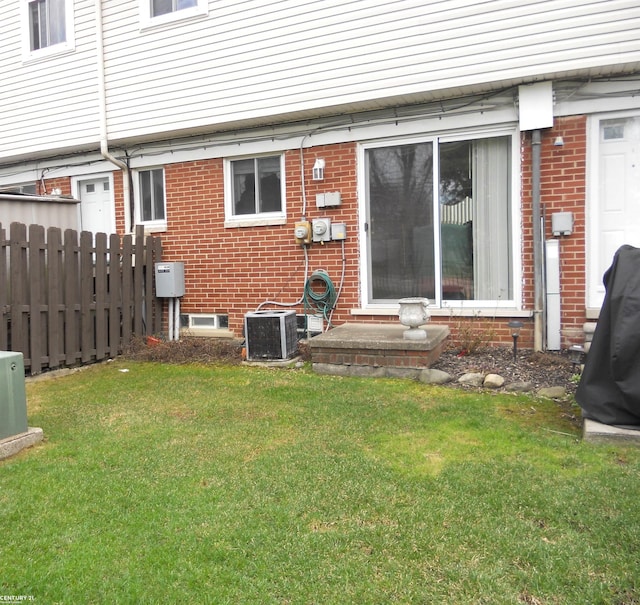 back of property featuring a yard, brick siding, central AC, and fence