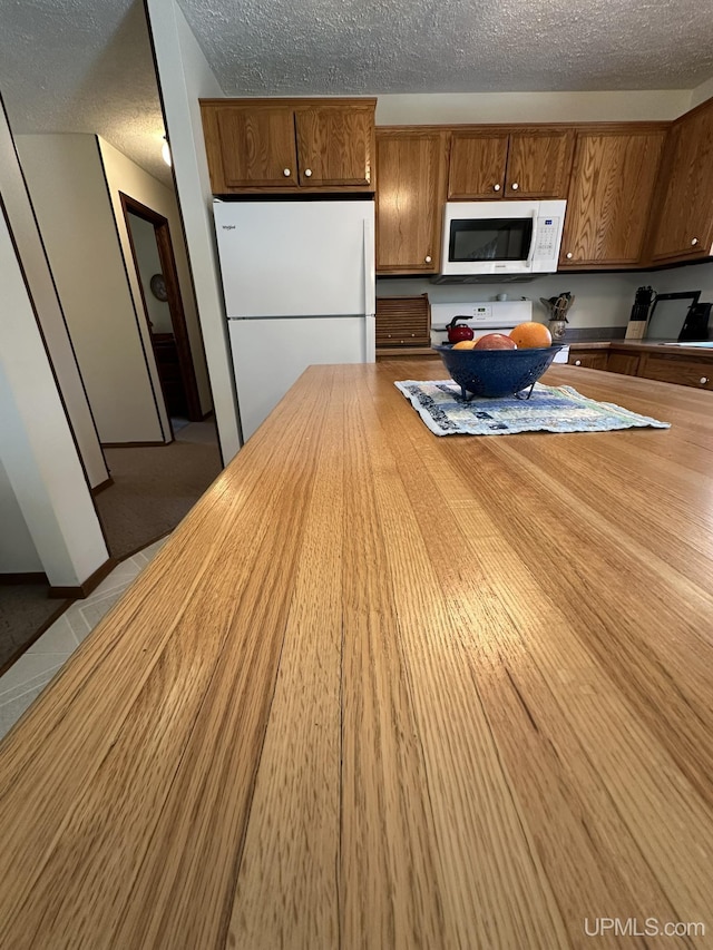kitchen with brown cabinetry, a textured ceiling, butcher block counters, and white appliances