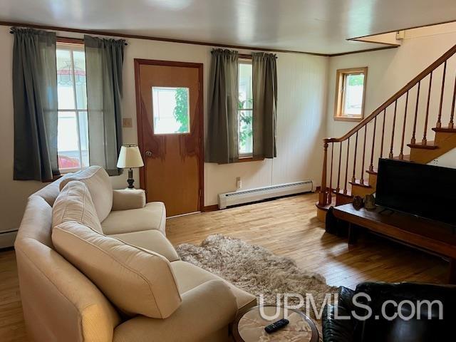 living area with ornamental molding, baseboard heating, stairway, and wood finished floors