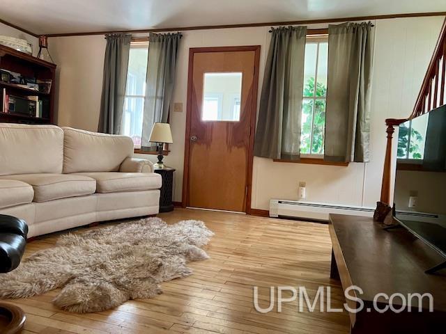 living room featuring ornamental molding, baseboard heating, and hardwood / wood-style floors