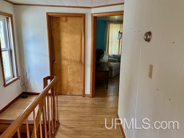 corridor featuring light wood-style floors, ornamental molding, and an upstairs landing