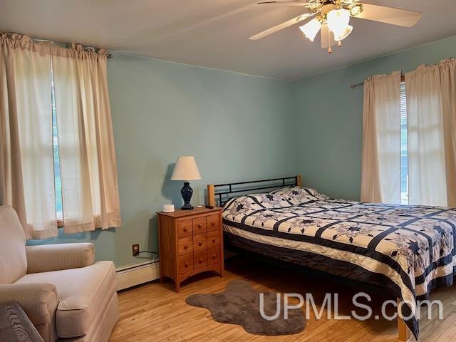 bedroom with light wood finished floors, ceiling fan, and baseboard heating