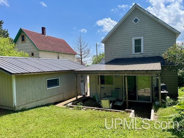 back of property featuring a lawn, a patio, and metal roof