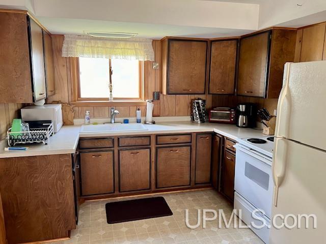 kitchen featuring white appliances, brown cabinetry, a sink, and light countertops