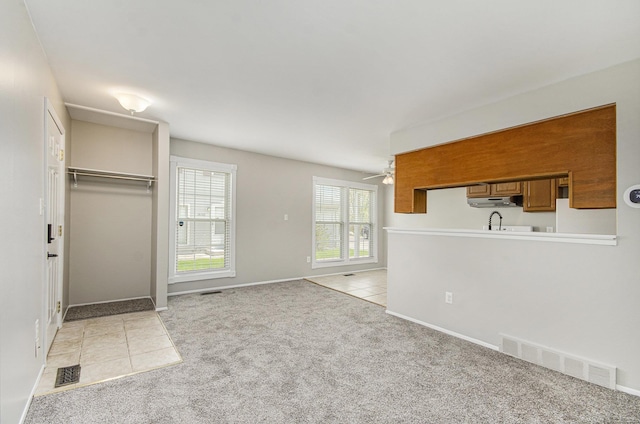 unfurnished living room with light carpet, a ceiling fan, baseboards, light tile patterned floors, and visible vents