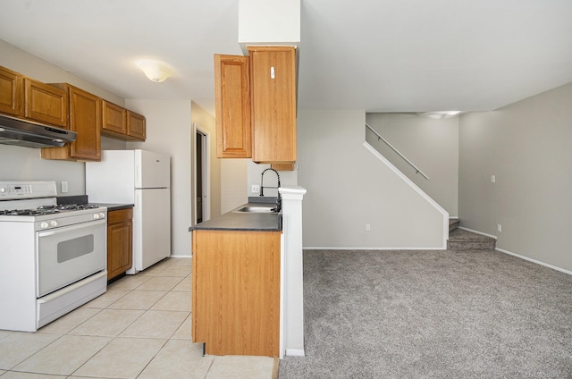 kitchen featuring brown cabinetry, a sink, baseboards, under cabinet range hood, and white appliances