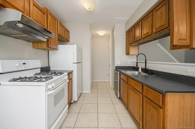 kitchen featuring brown cabinetry, dark countertops, a sink, under cabinet range hood, and white appliances