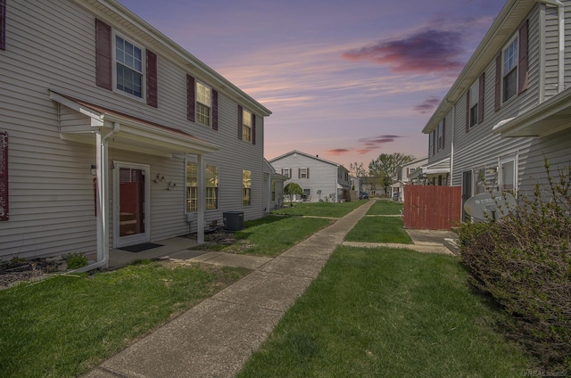 property exterior at dusk with a lawn, central AC, and a residential view
