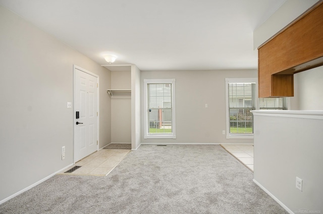 unfurnished living room with light tile patterned floors, baseboards, light carpet, and a wealth of natural light