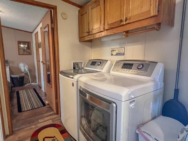 washroom with separate washer and dryer, a textured ceiling, cabinet space, and light wood finished floors