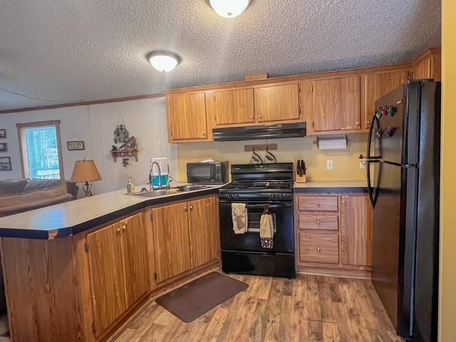 kitchen with a sink, a peninsula, black appliances, light wood-type flooring, and under cabinet range hood