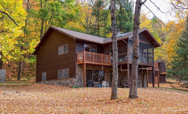 rear view of property featuring a deck, stone siding, a wooded view, a sunroom, and log veneer siding