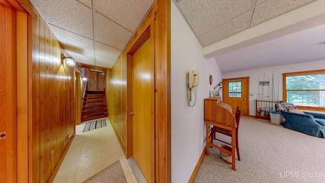 hallway featuring light carpet, wood walls, stairs, and baseboards