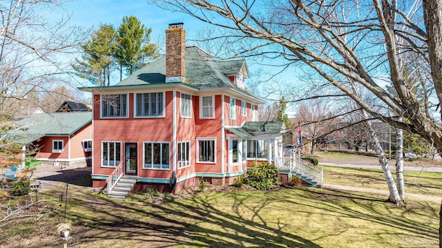 back of property featuring a chimney, entry steps, a shingled roof, and a lawn