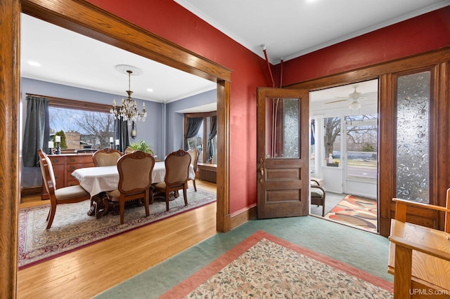 foyer entrance featuring crown molding, light carpet, baseboards, and ceiling fan with notable chandelier