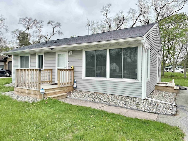 rear view of house with a shingled roof, a yard, and a wooden deck