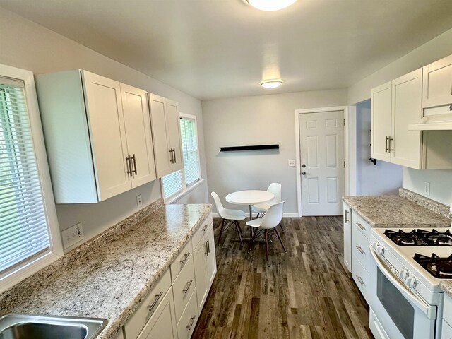 kitchen with gas range gas stove, light stone countertops, under cabinet range hood, dark wood-type flooring, and white cabinets
