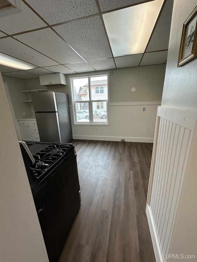 kitchen featuring freestanding refrigerator, a wainscoted wall, a paneled ceiling, dark wood finished floors, and gas stove