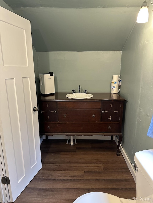 half bath featuring toilet, lofted ceiling, vanity, and wood finished floors
