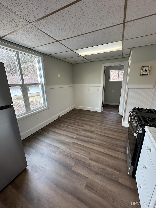 interior space with a wainscoted wall, freestanding refrigerator, dark wood-type flooring, a paneled ceiling, and baseboards
