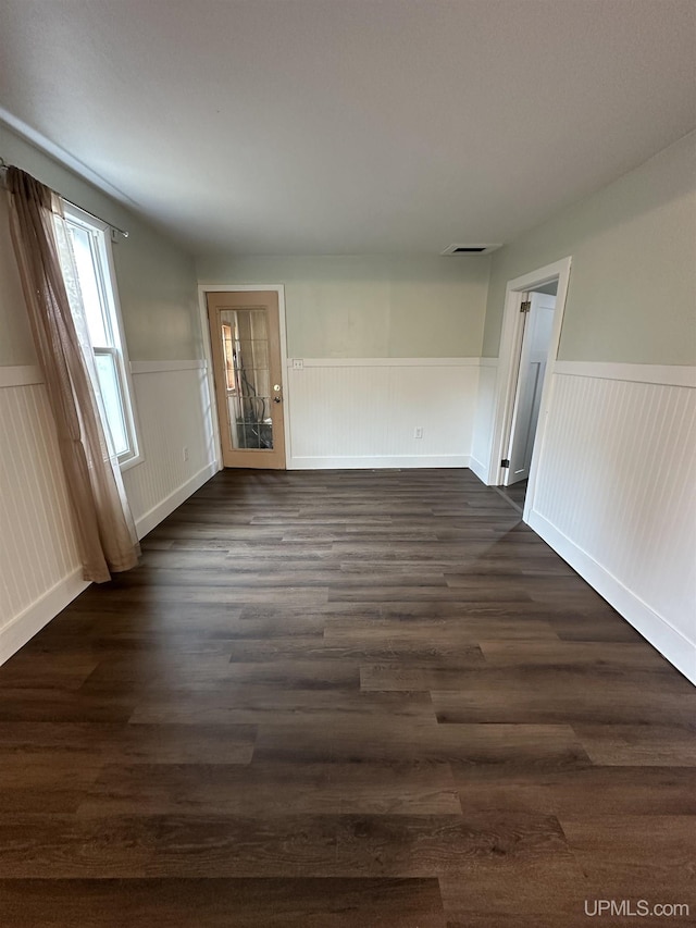empty room with wainscoting, visible vents, and dark wood-style floors