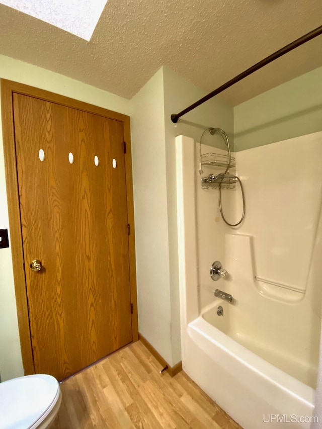 bathroom featuring toilet, wood finished floors, shower / bathing tub combination, and a textured ceiling