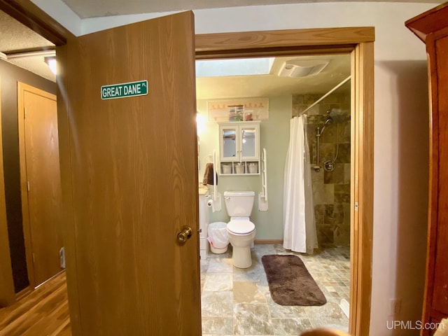 full bath featuring toilet, stone finish flooring, and a tile shower