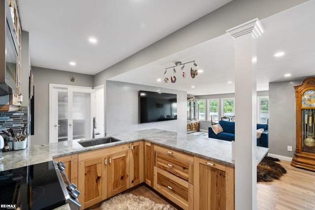 kitchen featuring a sink, stainless steel range with electric stovetop, light stone counters, ornate columns, and light wood-style flooring