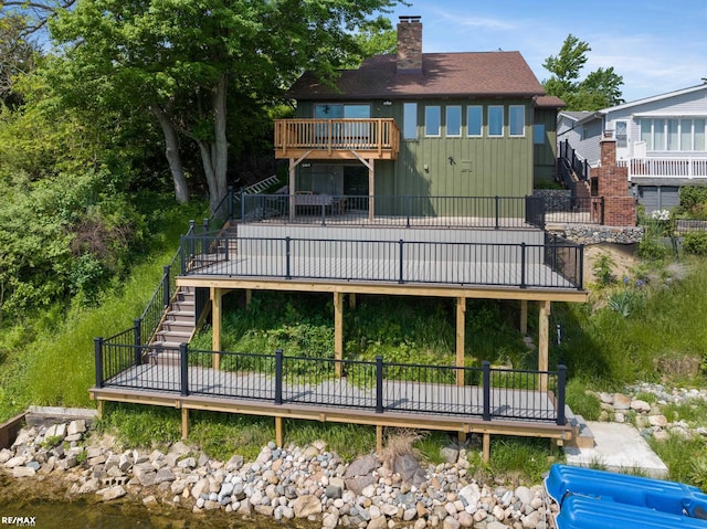 rear view of property with a chimney, a wooden deck, board and batten siding, a balcony, and stairs