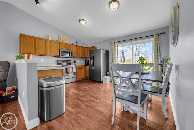 kitchen featuring lofted ceiling, baseboards, wood finished floors, light countertops, and appliances with stainless steel finishes