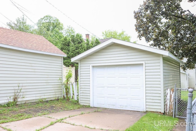 detached garage featuring concrete driveway and fence