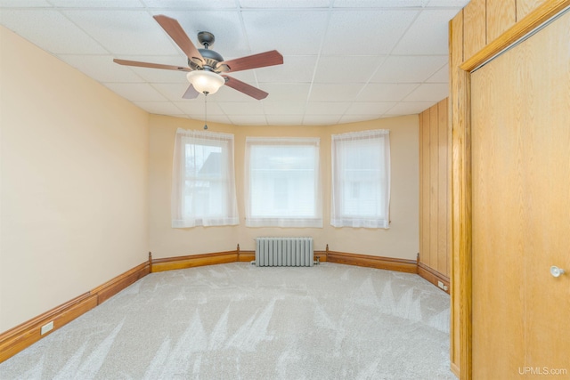empty room featuring radiator, carpet flooring, a drop ceiling, and ceiling fan