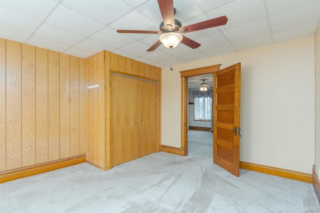 unfurnished bedroom with carpet flooring, a drop ceiling, a closet, wood walls, and baseboards