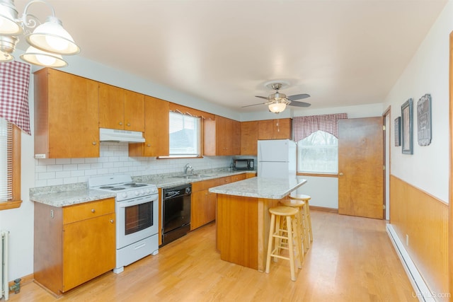 kitchen featuring a sink, black appliances, under cabinet range hood, a baseboard radiator, and light wood finished floors