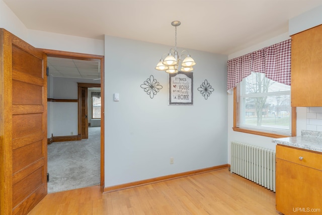 unfurnished dining area with an inviting chandelier, a drop ceiling, radiator, baseboards, and light wood-style floors