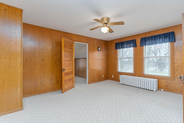 empty room featuring carpet floors, wooden walls, a ceiling fan, and radiator heating unit