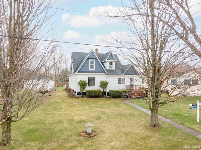 cape cod-style house with fence, a wooden deck, a chimney, a front yard, and roof with shingles