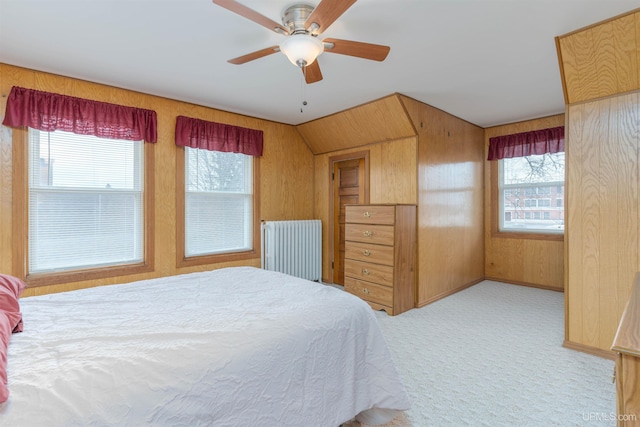 carpeted bedroom featuring multiple windows, wood walls, a ceiling fan, and radiator heating unit