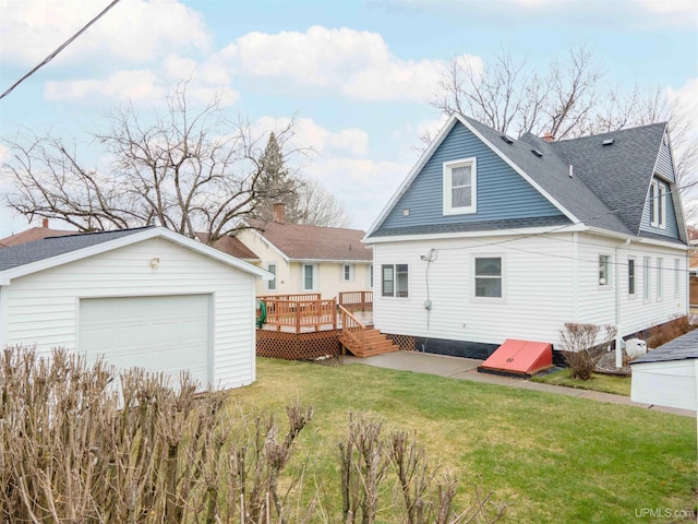 back of property featuring a garage, a lawn, a wooden deck, an outbuilding, and roof with shingles