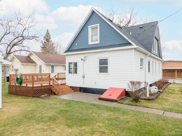 rear view of house with a yard, a patio area, a wooden deck, and roof with shingles