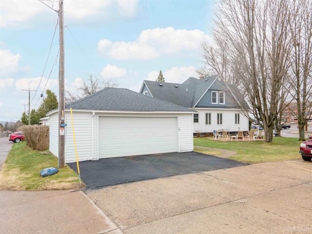 view of front of property with a detached garage, a shingled roof, a front lawn, and an outbuilding